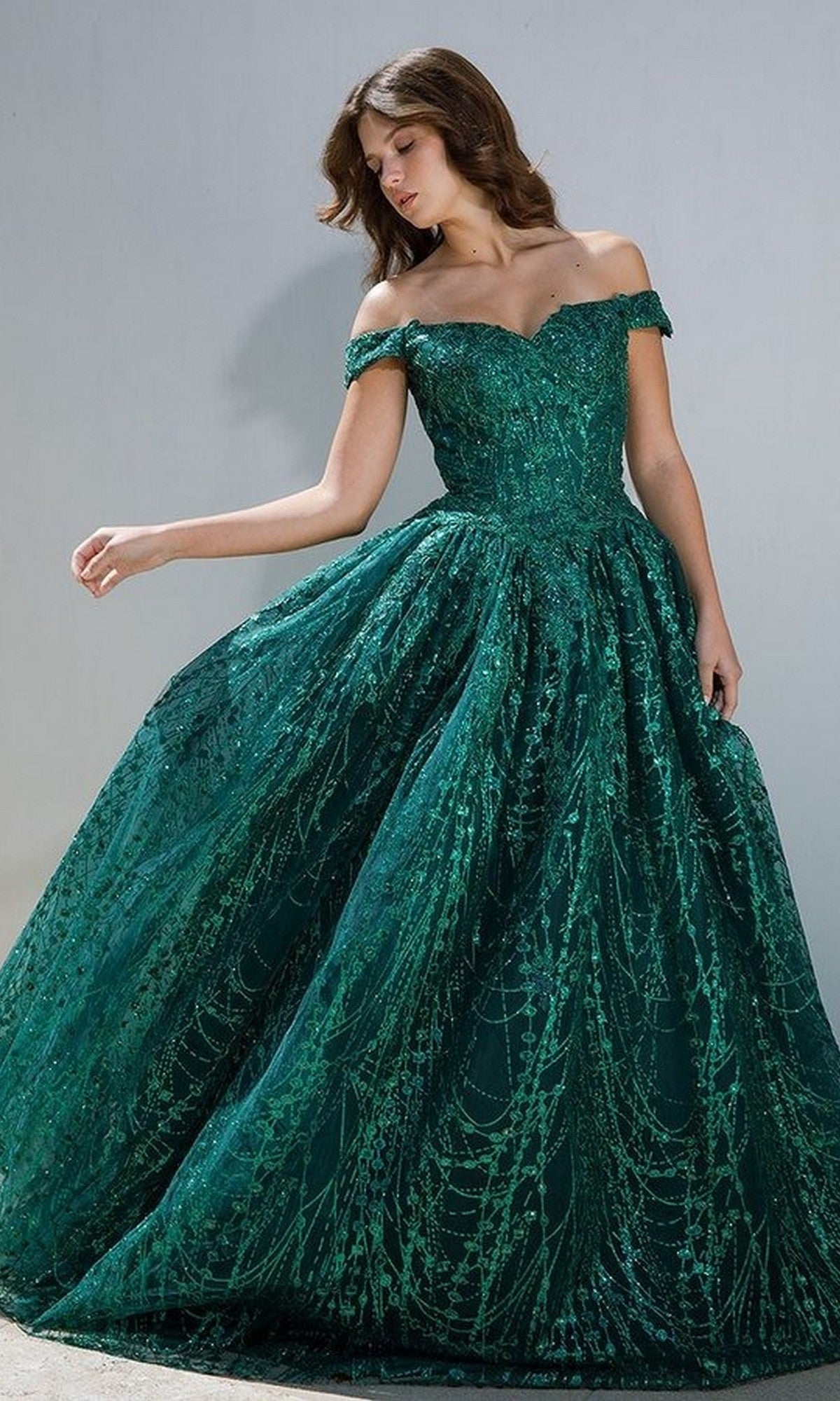 A woman models the Eureka 9778 Long Prom Dress in emerald green, featuring off-the-shoulder design with intricate lace and sequin details, against a plain light background.